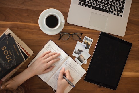 Person writing at desk next to laptop